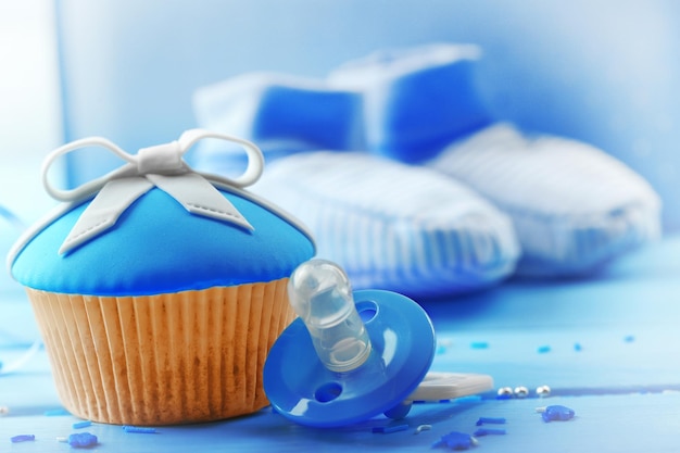 Tasty cupcake with bow and baby shoes on color wooden background