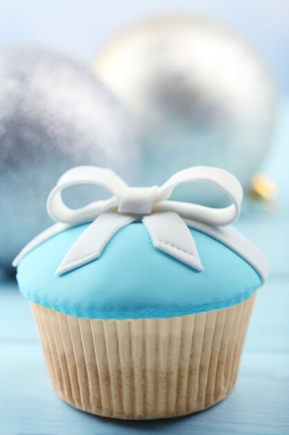 Tasty cupcake with bow and Christmas toys on color wooden background