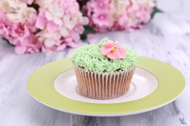 Tasty cupcake with butter cream on plate on color wooden background