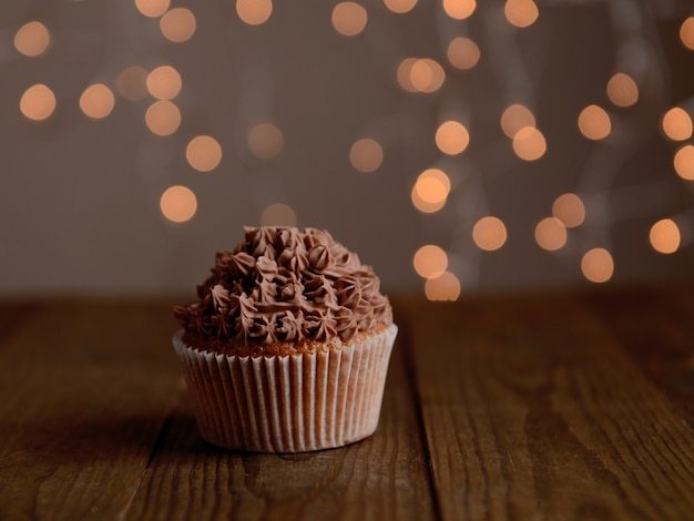 Tasty cupcake with butter cream, on wooden table with defocused lights