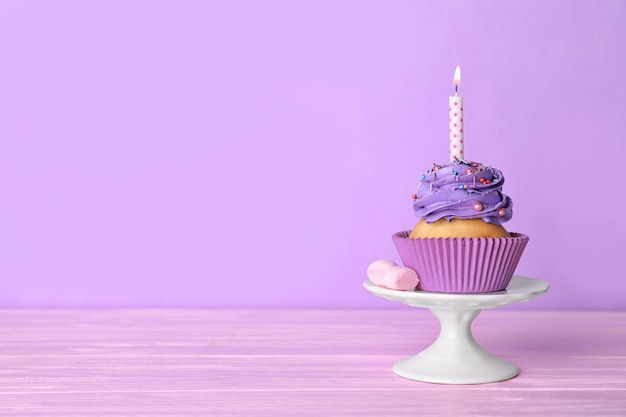 Tasty cupcake with candle on table against color background