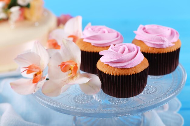 Tasty cupcakes on stand and cake on table on color background