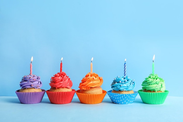 Tasty cupcakes with candles on color background