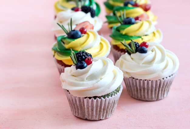 Tasty cupcakes with cream cheese topped with fresh berries Pink background