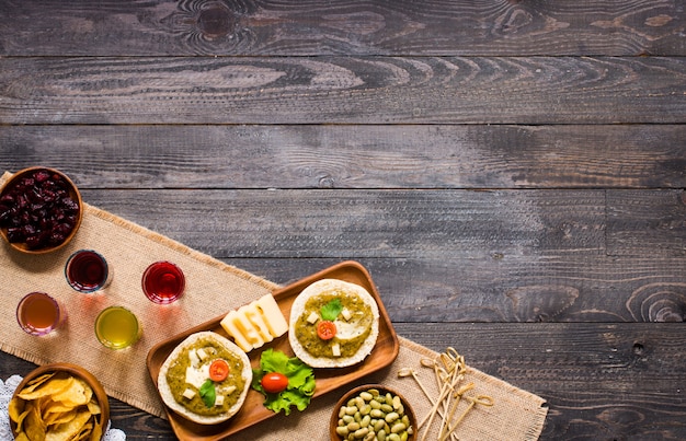 Tasty and delicious bruschetta with avocado, tomatoes, cheese, herbs, chips and liquor, on a wooden background.