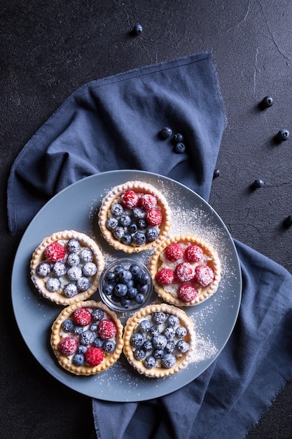 Tasty dessert with fresh blueberries and raspberries on a large gray plate. Black background.