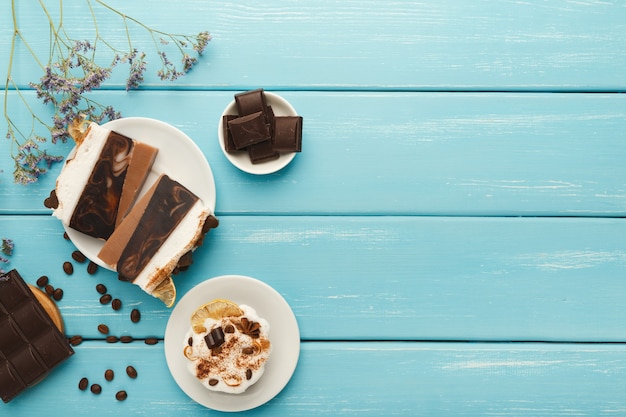 Sfondo di gustosi dessert. varie torte e barrette di cioccolato su tavolo rustico blu con chicchi di caffè sparsi e fiori viola, stile provenzale, vista dall'alto, spazio copia
