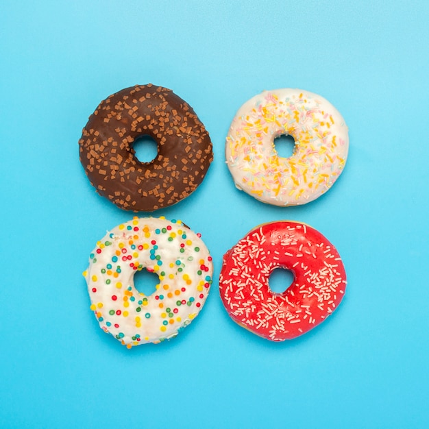 Tasty donuts of different types on a blue space. Concept of sweets, bakery, pastries. Square. Flat lay, top view.