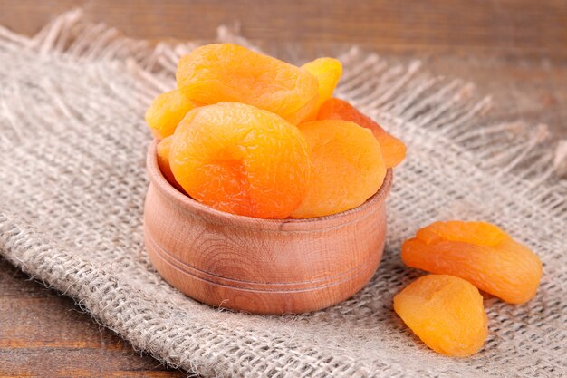 Photo tasty dried apricots in a wooden bowl closeup on a brown wooden background