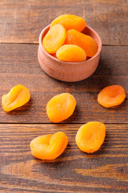 Tasty dried apricots in a wooden bowl closeup on a brown wooden background
