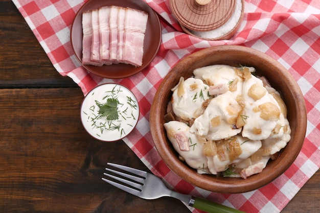 Tasty dumplings with fried onion in brown bowl on wooden background