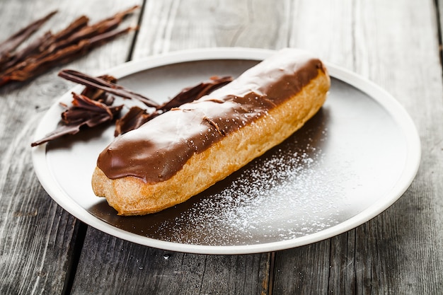 오래 된 나무 테이블에 서있는 접시에 초콜릿 크림과 함께 맛있는 eclair