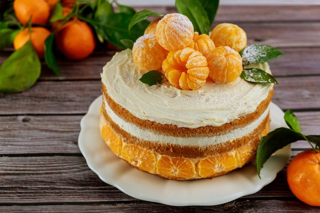 Tasty festive cake with peeled mandarins and green leaves.