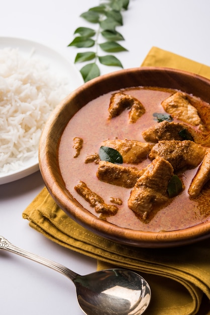 Tasty fish curry served with white cooked basmati rice with curry leaves in the background, favourite coastal indian food