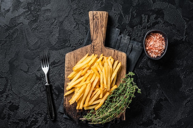 Tasty french fries on wooden cutting board. Black background. Top view.