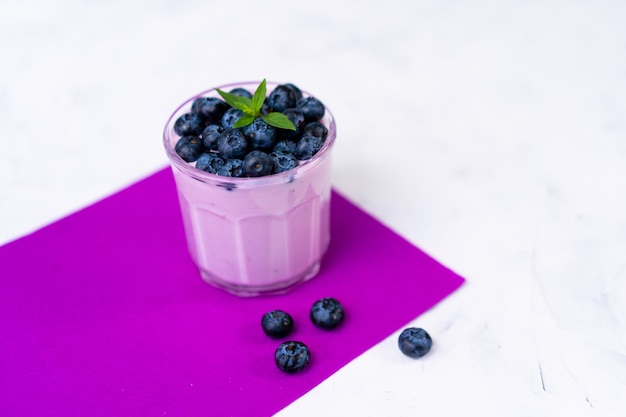 Tasty fresh blueberry yoghurt shake dessert in glass standing on white table purple napkin . Homemade berry smoothie. Healthy eating. Diet food yogurt