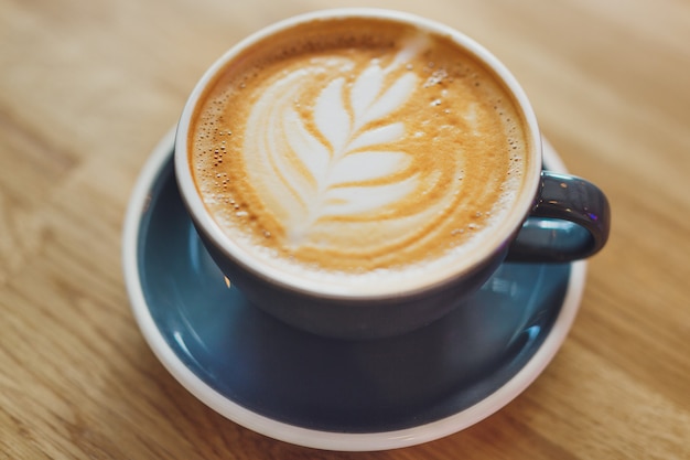 Tasty fresh cappuccino in cup on wooden table. Closeup