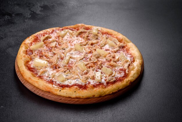 Tasty fresh oven pizza with tomatoes, cheese and pineapple on a dark concrete background