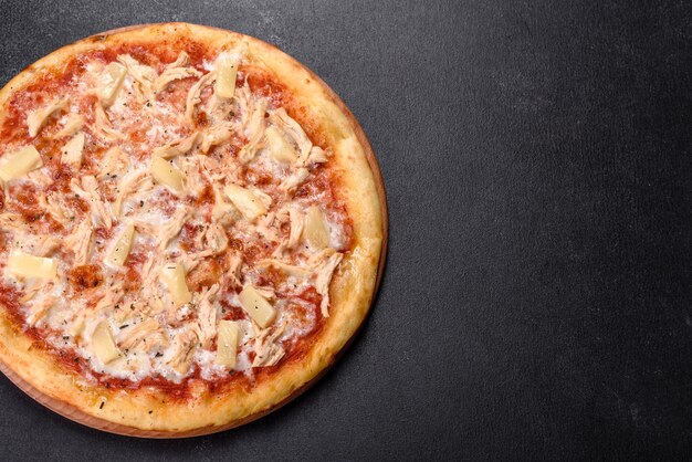 Tasty fresh oven pizza with tomatoes, cheese and pineapple on a dark concrete background