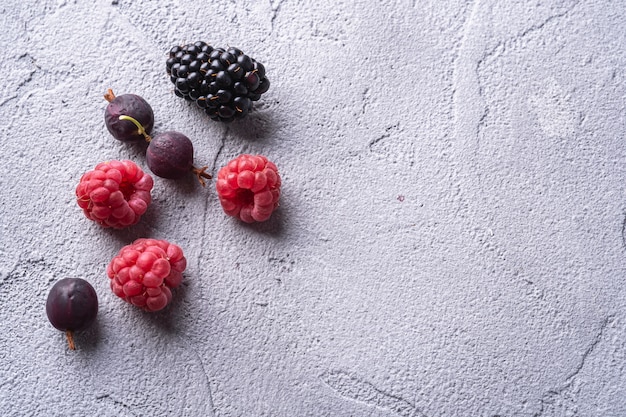 Photo tasty fresh ripe raspberry, blackberry, gooseberry and red currant berries, healthy food fruit on stone concrete table, angle view macro copy space