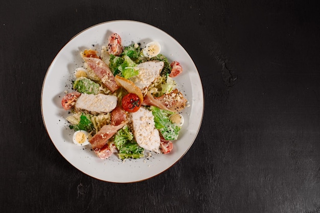 Tasty fresh salad ceasar with ham and vegetables on black background