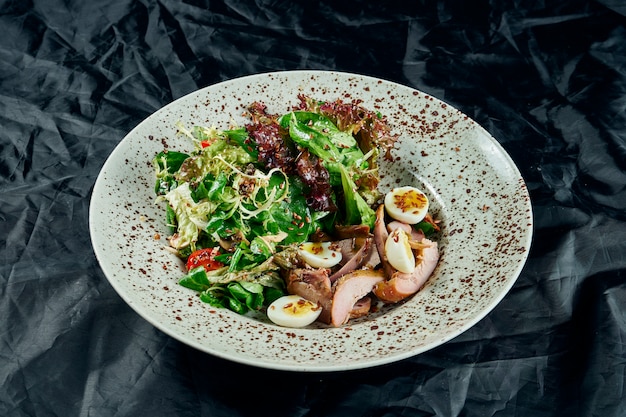 Tasty, fresh Salad with duck breast, spinach, quinoa, quail eggs and cherry tomatoes in a white bowl on a black table. Healthy Fitness Nutrition. Close up food