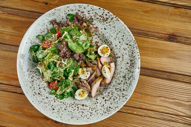 Insalata saporita e fresca con petto d'anatra, spinaci, quinoa, uova di quaglia e pomodori ciliegia in una ciotola bianca su una tavola di legno. nutrizione sana di forma fisica. close up food