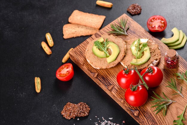 Tasty fresh sandwich with liver paste, avocado pieces and a arugula on a dark concrete table