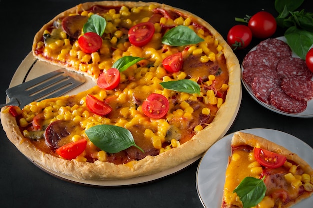 Tasty freshly prepared pizza with cherry tomatoes and green basil on a black background