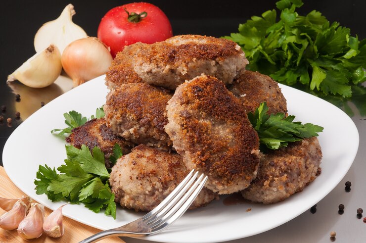 Фотография вкусные жареные мясные котлеты, украшенные овощами и зеленью