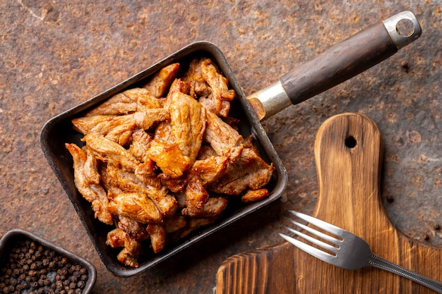 Foto gustoso filetto di maiale fritto in una vecchia padella su sfondo con texture arrugginita vista tavolo dall'alto piatto