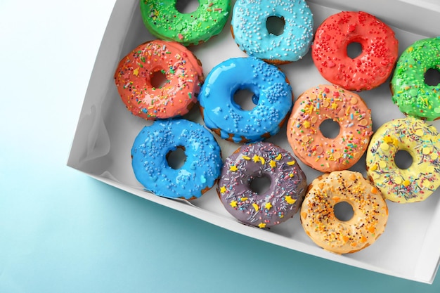 Tasty glazed donuts in box on color background