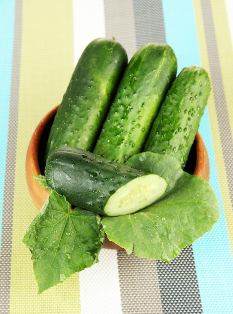 Tasty green cucumbers in wooden bowl on bright background