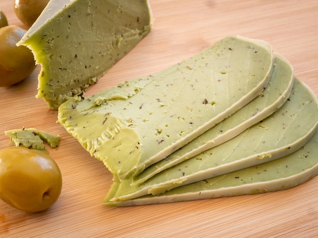 Tasty green pesto cheese and olives on a wooden cutting board close up