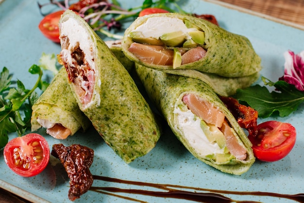 Tasty green rolls filled with salmon and cheese on wooden background