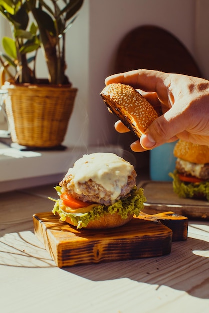 Tasty grilled cheeseburger with lettuce and tomato served on a rustic wooden board. Man cooks on the kitchen