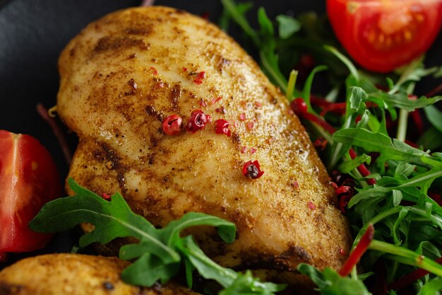 Tasty grilled chicken breast with vegetables and salad served on dark table. Closeup.