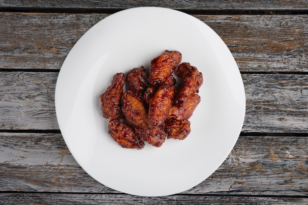 Tasty grilled chicken wings Buffalo on a white dish on wooden table, top view