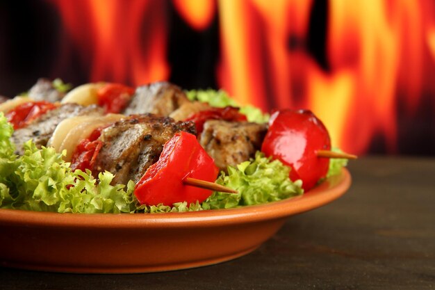 Фото Вкусное мясо на гриле и овощи на тарелке на фоне огня