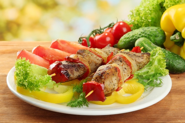 Tasty grilled meat and vegetables on skewer on plate on wooden table