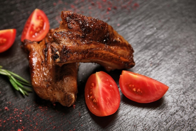 Tasty grilled ribs with slices of fresh tomato on dark background