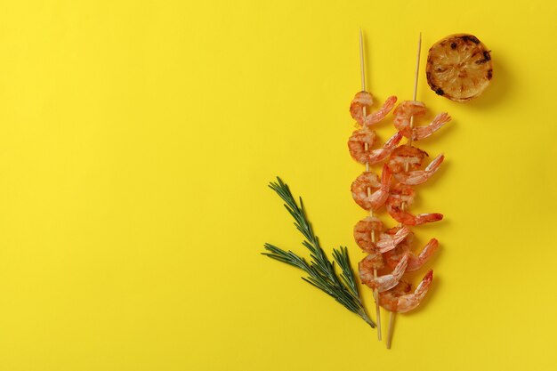 Tasty grilled shrimps skewers on yellow background