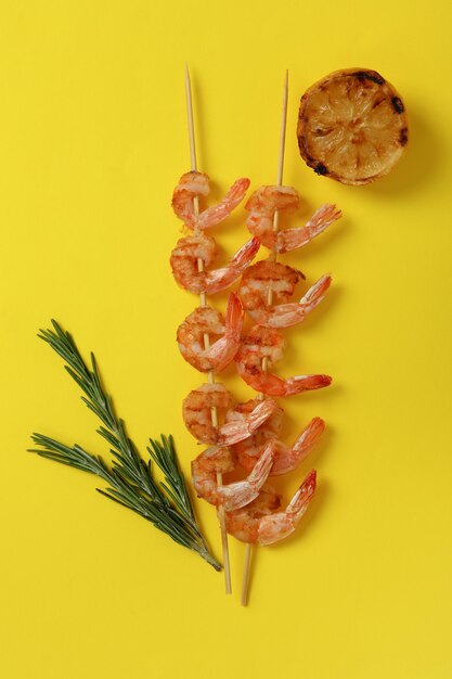 Tasty grilled shrimps skewers on yellow background