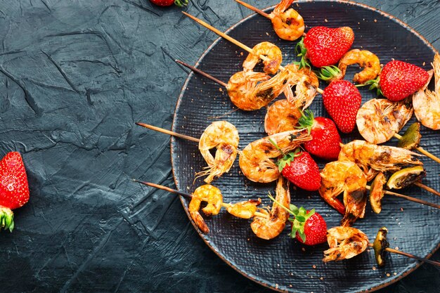 Tasty grilled shrimps on wooden skewers with strawberries.Roasted shrimps or prawns