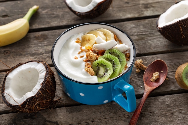 Tasty and healthy breakfast. Bowl fruit coconut yogurt with granola on wooden table. Healthy vegan food concept