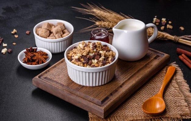 Tasty healthy breakfast with cereals granola chocolate milk and jam on a dark concrete background