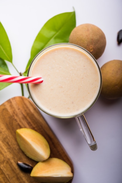 Tasty and healthy Chickoo, Chikoo OR Sapota Milkshake. It's a healthy fruit mixed with Milk and ice served in a glass over colourful or wooden background. Selective focus