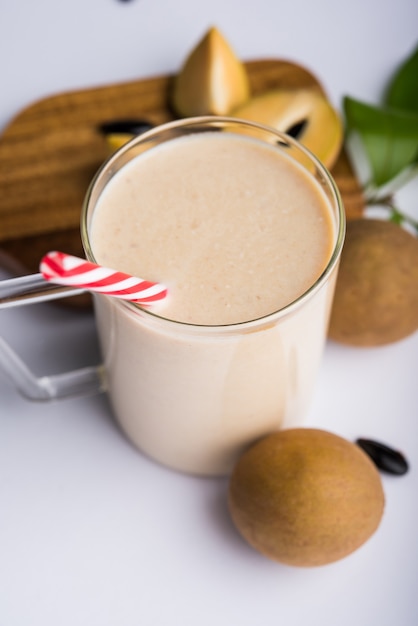 Tasty and healthy Chickoo, Chikoo OR Sapota Milkshake. It's a healthy fruit mixed with Milk and ice served in a glass over colourful or wooden background. Selective focus