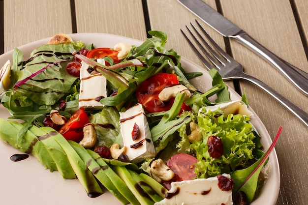 Tasty and healthy salad with arugula, brie, cheese, avocado, cherry tomatoes, dry cranberry and cashews.