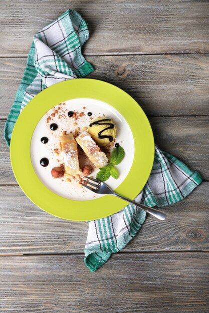 Tasty homemade apple strudel with nuts, mint leaves and ice-cream on plate, on wooden background